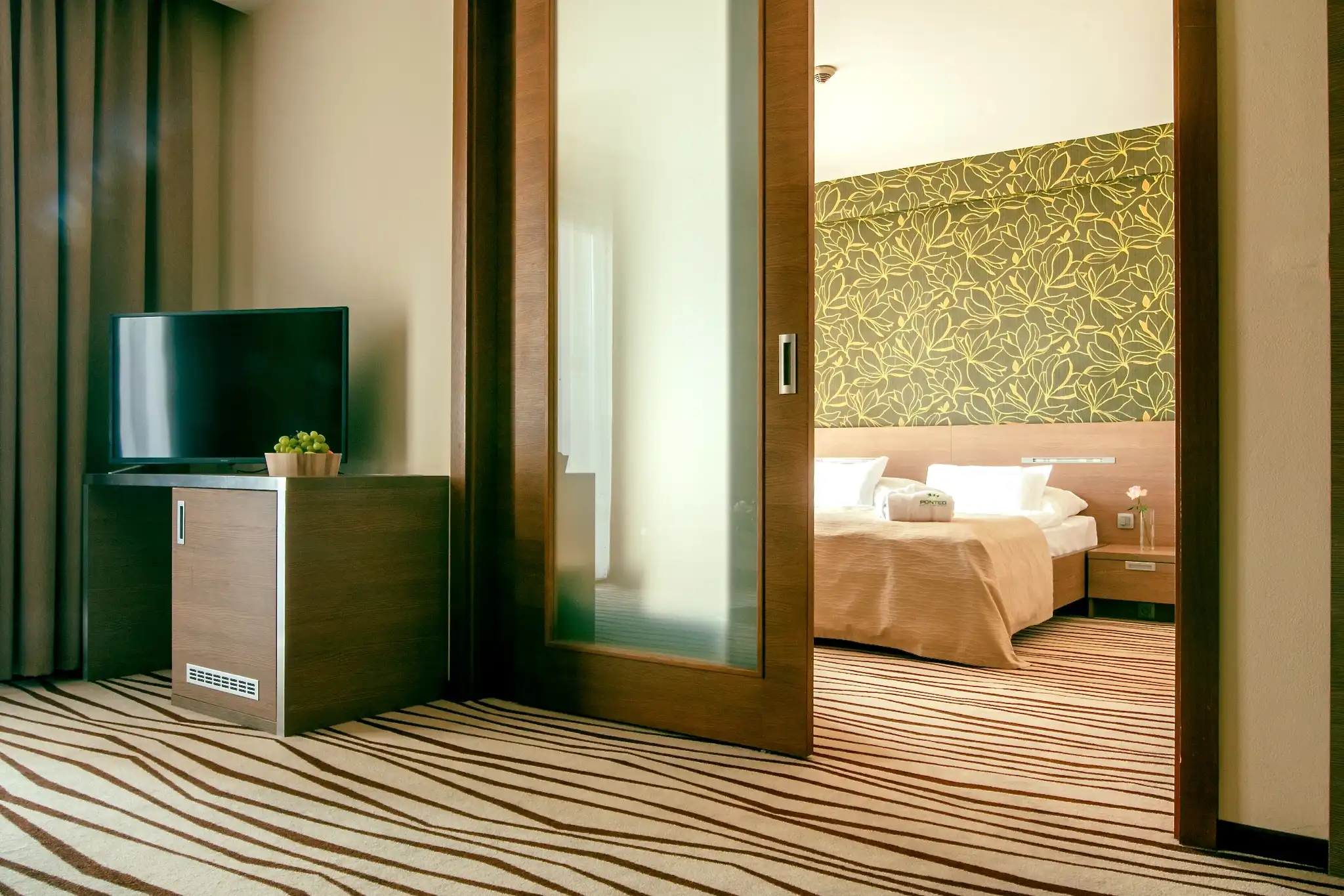 Apartmán hotela Ponteo**** Rusovce s kobercom, závesmi a rastlinným vzorom za posteľou