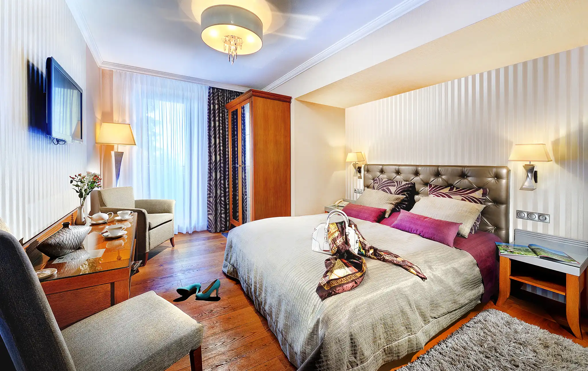 Izba Deluxe Grandhotela Praha s pruhovanými stenami, bielymi záclonami a fialovými textilnými akcentmi